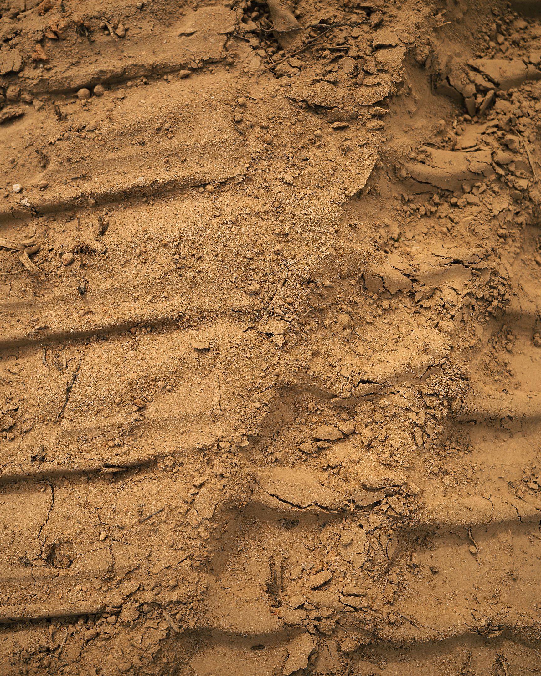 Tire tracks pressed into dry red clay on a job site